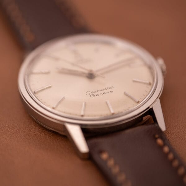 Close-up of an Omega Automatic Seamaster Geneve Double Signed Dial Ref. 165.002 with a brown leather strap on a brown surface.
