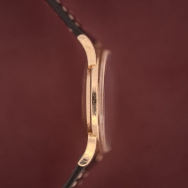 Side view of a Girard Perregaux Gyromatic 10k gold filled case wristwatch with a cream dial and brown leather strap, set against a maroon background.