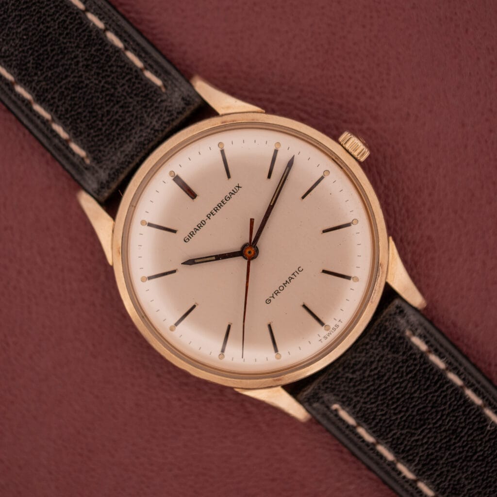 A Girard Perregaux Gyromatic with a 10k gold filled case and cream dial rests elegantly on a burgundy surface.