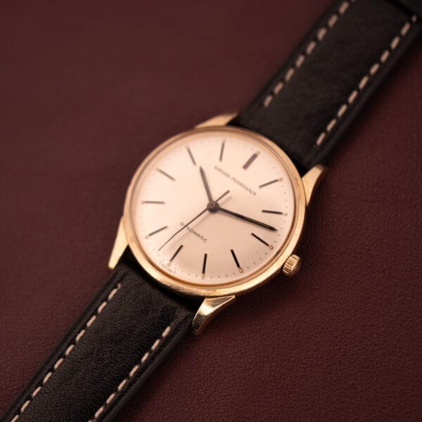 A Girard Perregaux Gyromatic with a 10k gold filled case and cream dial is elegantly displayed on a dark brown leather surface.