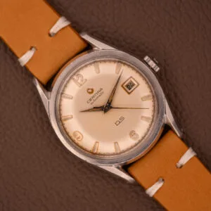 1959 Certina DS Automatic Date 1st Edition with Cal. 25-451 stainless steel case, tan leather strap, displayed on a brown surface showing 7:22 and date 24.