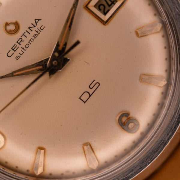 Close-up of a 1959 Certina DS Automatic Date 1st Edition in stainless steel, featuring gold hour markers, Cal. 25-451 movement, and a date window at 3 o’clock.