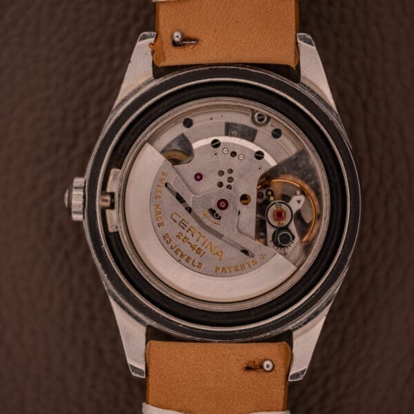 Close-up of a 1959 Certina DS Automatic Date 1st Edition Stainless Steel watch, showcasing its exposed Cal. 25-451 mechanical movement and gears, paired with a tan leather strap.