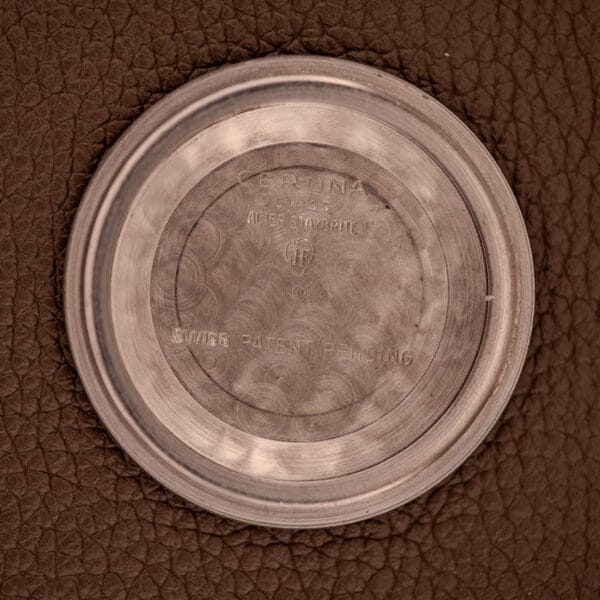 A 1959 Certina DS Automatic Date 1st Edition stainless steel case back on brown leather, engraved RETINA SWISS PATENT PENDING, from Cal. 25-451.