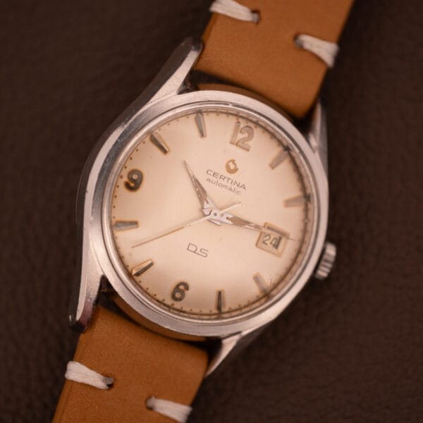 1959 Certina DS Automatic Date 1st Edition in stainless steel, powered by Cal. 25-451, with tan leather strap and cream dial displaying the date as 24.