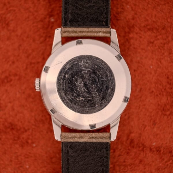 An Omega Automatic Stainless Steel Ref. 14773 Cream Dial Cal. 470 with a black leather strap and engraved back rests on red fabric, featuring a worn black center detail.