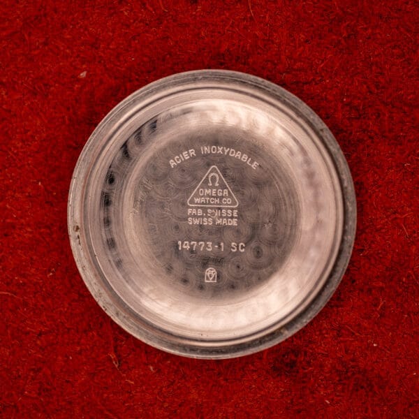 Omega Automatic Stainless Steel Ref. 14773 Cal. 470 case back with engraved markings, displayed on a red textured background. Features a Cream Dial and stainless steel build for timeless elegance.