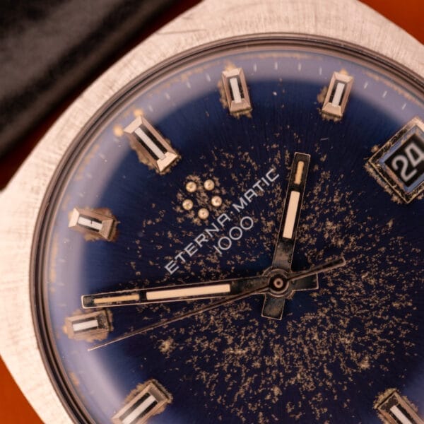 Close-up of the Eterna Matic 1000 Blue Patina Dial 110T watch, featuring a worn blue patina dial, visible date at 3 o’clock, and classic stainless steel Cal. 1489K accents.