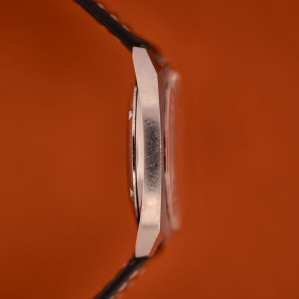 Side view of the Eterna Matic 1000 Blue Patina Dial 110T Stainless Steel Cal. 1489K wristwatch with a black strap, set against an orange background.