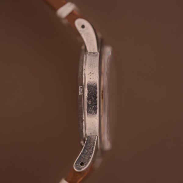 Side view of the Omega Automatic Seamaster Bumper "Türler Dial" Ref. 2576 with a worn silver case and brown leather strap, set against a warm brown background.