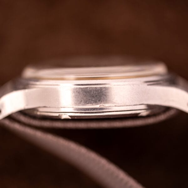 Close-up side view of the Omega Patina Dial Military "US ARMY" Ref. 2179, Stainless Steel Cal. 30T2 SC wristwatch case and strap set against a brown background—a classic once favored by the US Army.