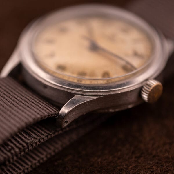 Close-up of an Omega Patina Dial Military "US ARMY" Ref. 2179 wristwatch with Cal. 30T2 SC, showing a worn dial and fabric strap on a brown surface.