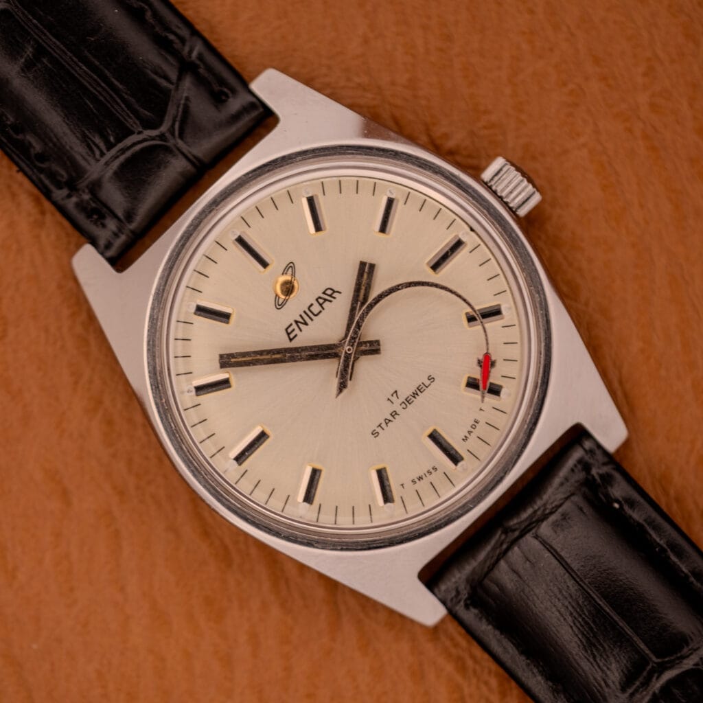 An Enciar Ocean Peal 17 Star Jewels "Space Ship Seconds" Ref. 2334 wristwatch with black leather strap is displayed elegantly on a brown textured surface.