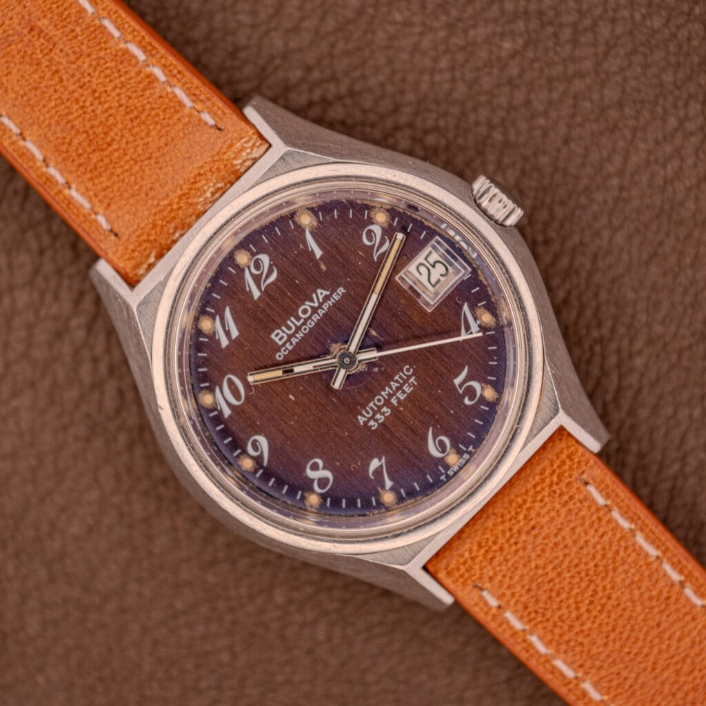 The Bulova Oceanographer Automatic 333 Feet features a blue/purple dial, date display, and an orange leather strap on brown leather. Model: Cal. 1132.10.