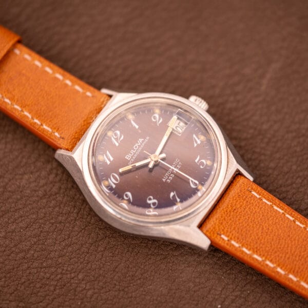 A vintage Bulova Oceanographer Automatic 333 Feet watch with a blue/purple dial (Cal. 1132.10) rests on a textured brown surface.