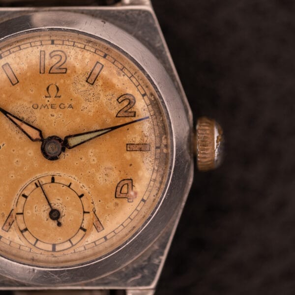 Close-up of a 1936 Omega Trench Watch, Cal. 23.4, featuring a worn beige dial with visible patina in a Hadley Staybrite Steel Case.