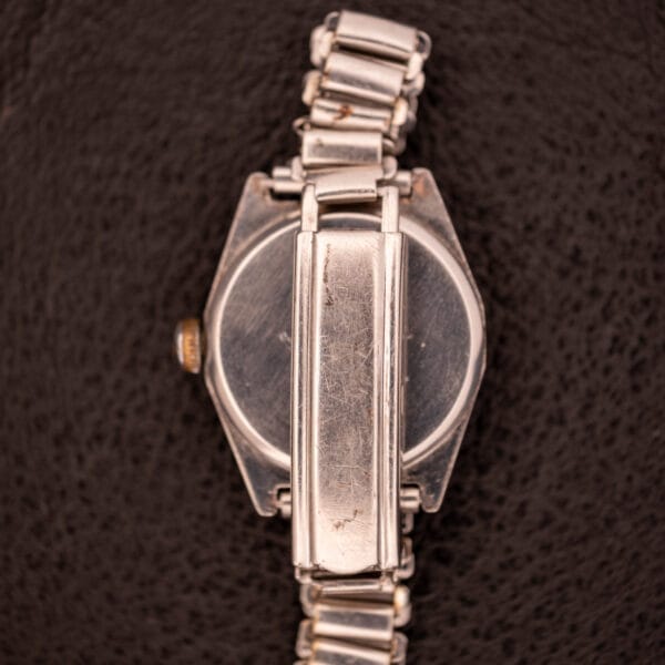 A 1936 Omega Trench Watch with a Hadley Staybrite Steel Case and metal band, Cal. 23.4, is shown from the back on a dark textured surface.