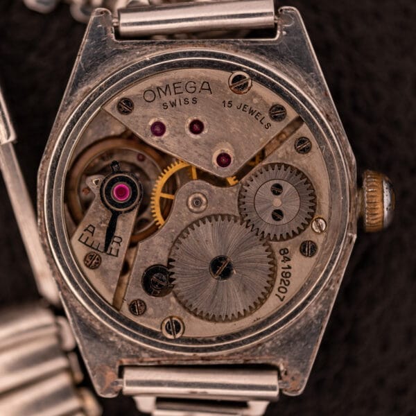 Close-up of the 1936 Omega Trench Watch movement with gears, screws, and 15 jewels engraved on its Cal. 23.4 mechanism, all housed in a Hadley Staybrite Steel Case.