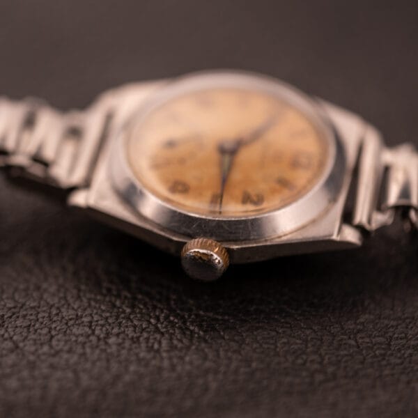 Close-up of a 1936 Omega Trench Watch with Hadley Staybrite Steel Case Cal. 23.4, featuring a faded, yellowed dial, resting on a dark surface.