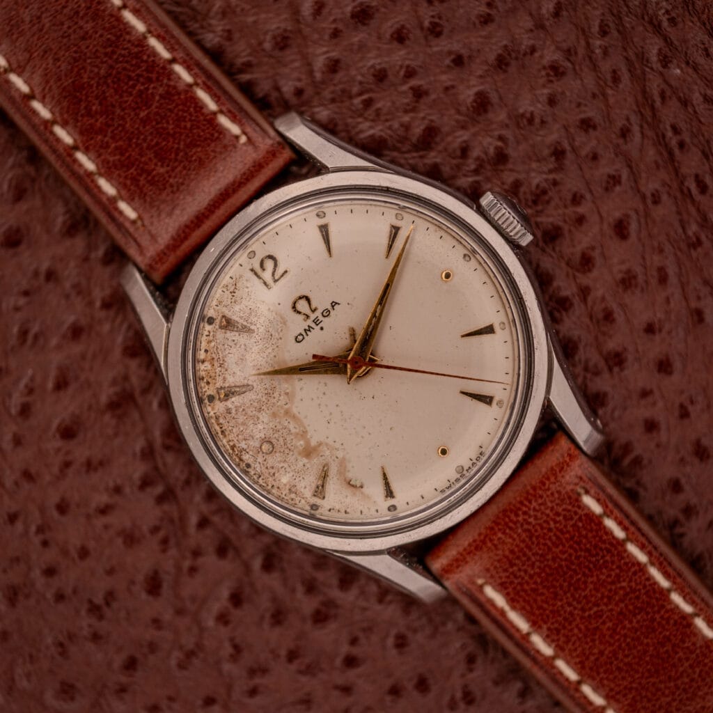 An Omega Jumbo Stainless Steel Ref. 2640 Manual Wind 283 Caliber wristwatch with a worn cream dial and brown leather strap, displayed on textured brown leather.
