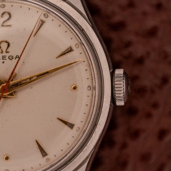 Close-up of the Omega Jumbo Stainless Steel Ref. 2640, featuring its dial, hands, crown, and manual wind 283 Caliber movement against a brown textured background.