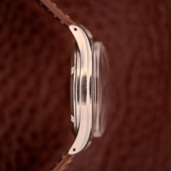 Side view of the Omega Jumbo Stainless Steel Ref. 2640 Manual Wind 283 Caliber wristwatch with a brown leather strap and steel case, set against a textured brown background.