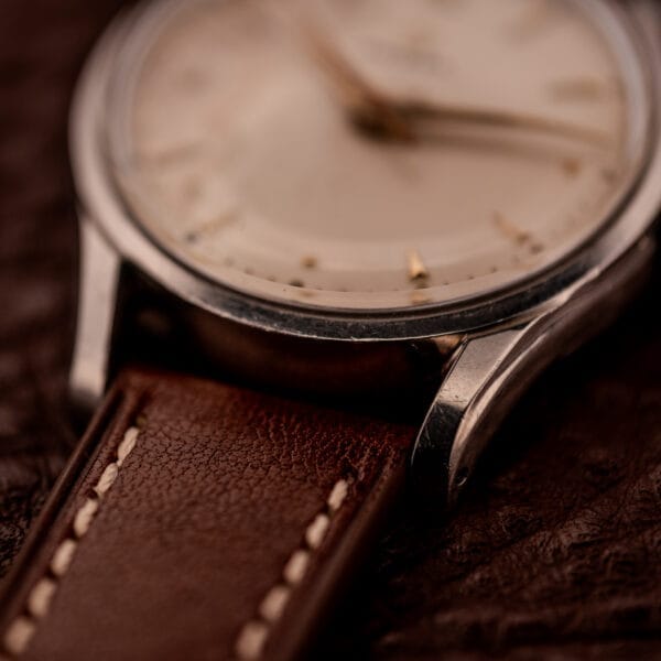 Close-up of an Omega Jumbo Stainless Steel Ref. 2640 wristwatch with manual wind 283 caliber and brown leather strap, displayed on a dark textured surface.