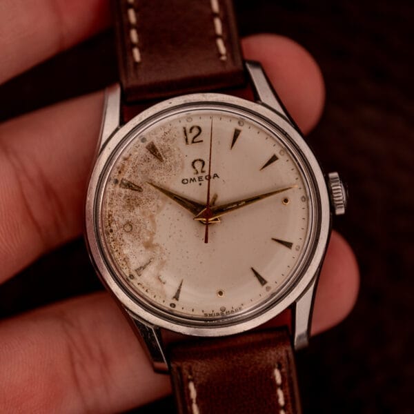 An Omega Jumbo Stainless Steel Ref. 2640 wristwatch, featuring a manual wind 283 caliber, brown leather strap, and a stained vintage white dial.