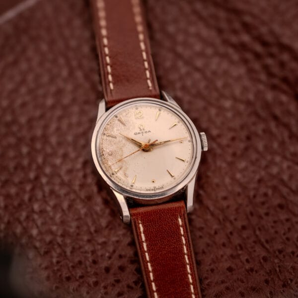The Omega Jumbo Stainless Steel Ref. 2640 Manual Wind 283 Caliber wristwatch, paired with a brown leather strap, is displayed on a textured brown surface.
