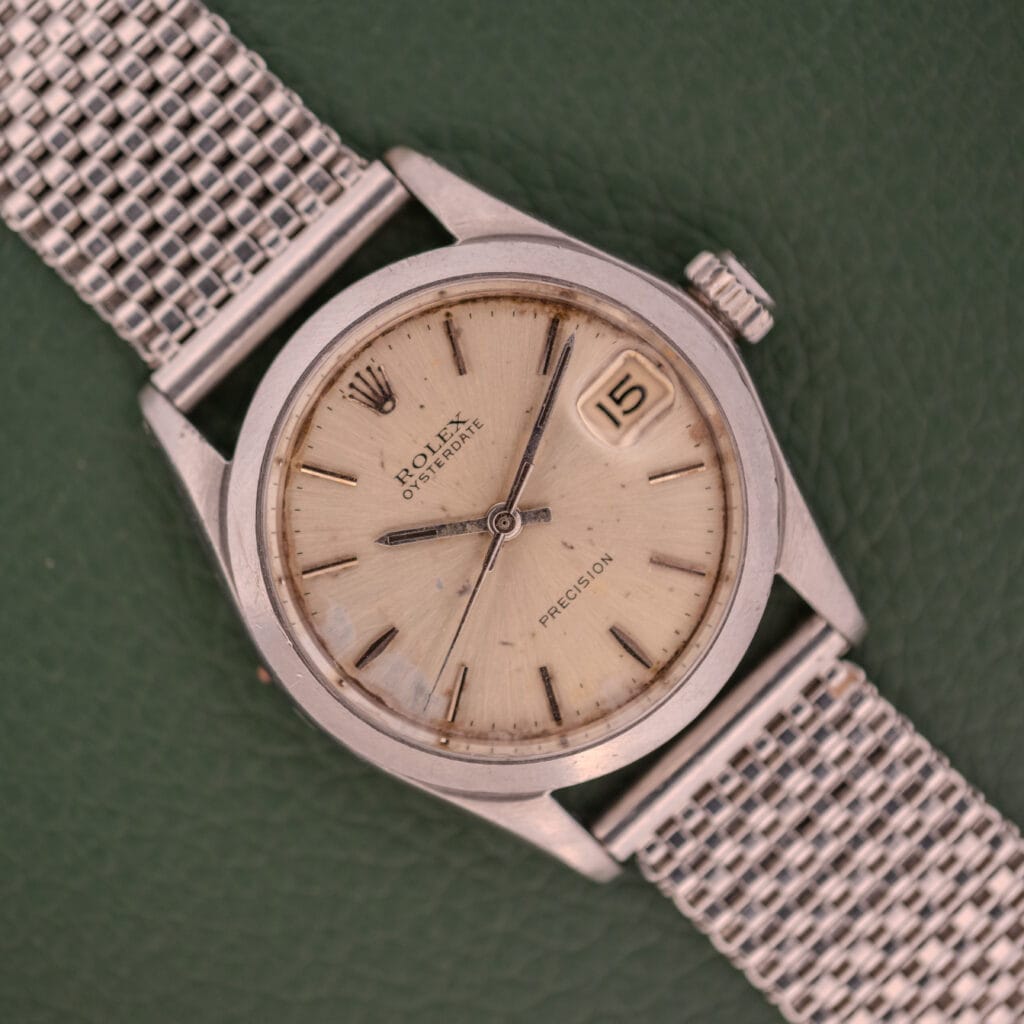 A Rolex Oysterdate Precision Ref. 6466 in stainless steel with a mesh strap displays the date as the 15th on a green background.