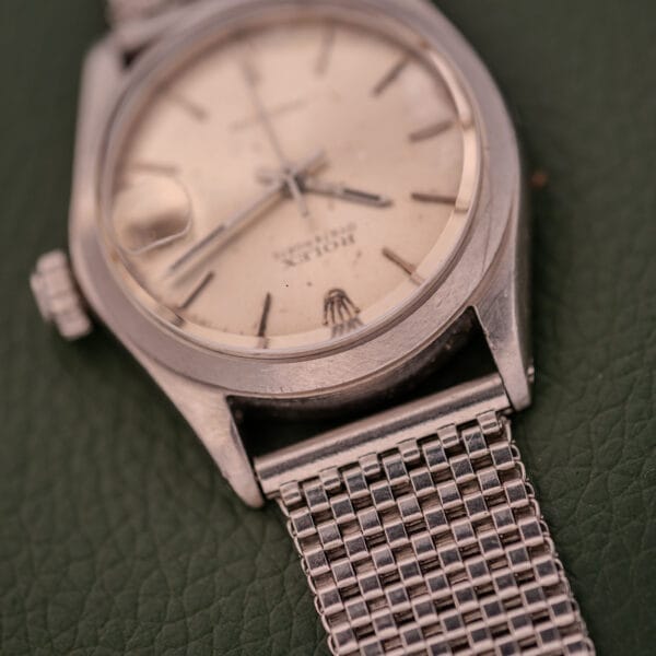 A Rolex Oysterdate Precision Ref. 6466 in stainless steel with a mesh band, displayed on a textured green surface.
