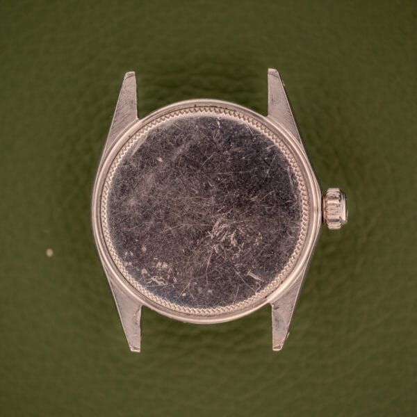 A scratched, empty Rolex Oysterdate Precision Ref. 6466 in stainless steel lies on a textured green background, with no dial or hands.