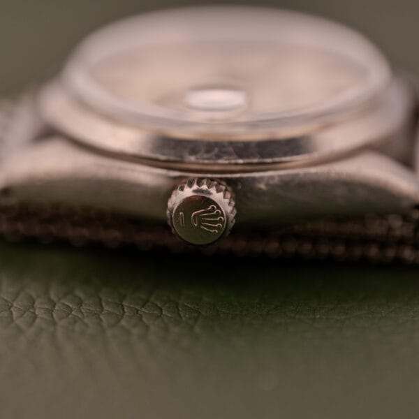 Close-up of the Rolex Oysterdate Precision Ref. 6466 crown with the Rolex logo, set on a textured green background. The stainless steel details emphasize the timeless elegance of this classic timepiece.