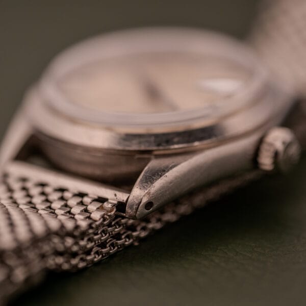 Close-up of a Rolex Oysterdate Precision Ref. 6466 in stainless steel, featuring a mesh band and worn, scratched lugs, displayed on a green surface.