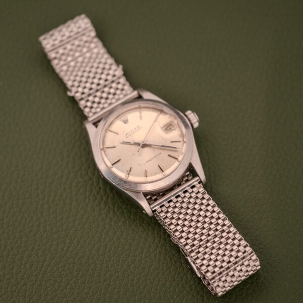 A Rolex Oysterdate Precision Ref. 6466 in stainless steel with a mesh band lies on a textured green surface.