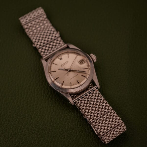 A Rolex Oysterdate Precision Ref. 6466 in stainless steel with a mesh band rests elegantly on a dark green textured surface.