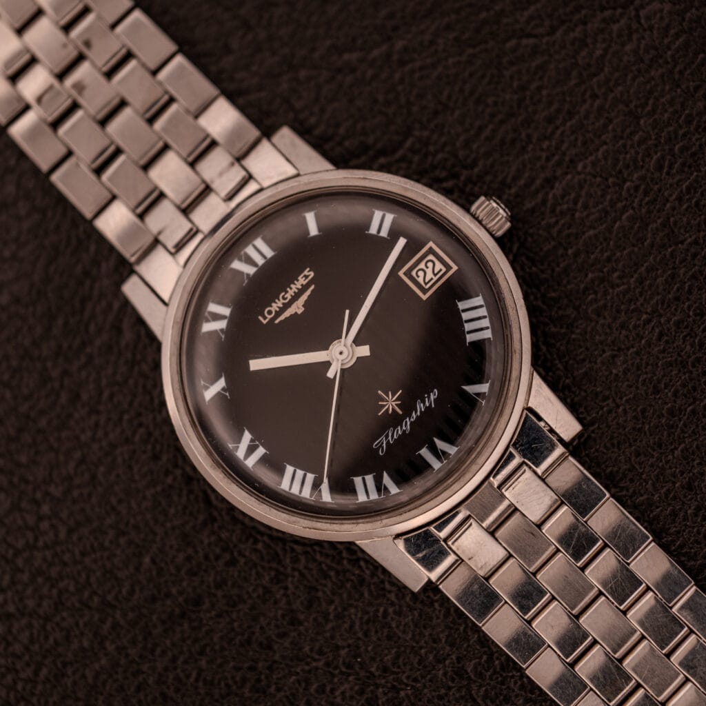A Longines Flagship Ref. 2821 wristwatch with a black "Pinstripe" dial and Diamond Cal. 285 rests on a brown textured surface.