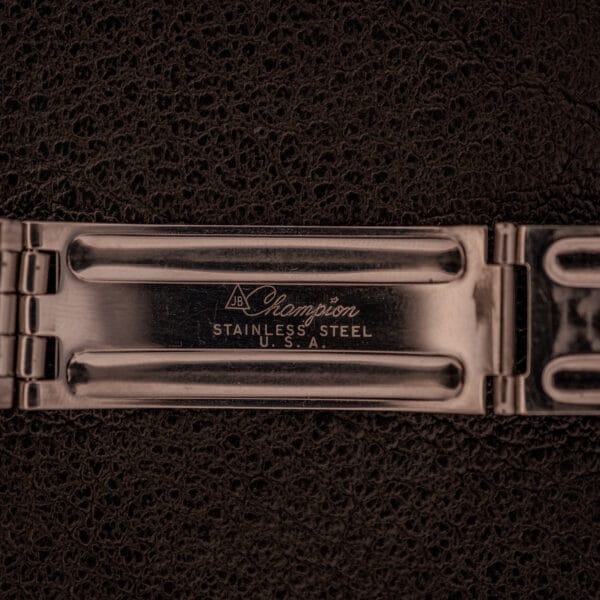 A close-up of a stainless steel watch clasp engraved with Champion Stainless Steel U.S.A., complementing the classic elegance of a Longines Flagship Ref. 2821 Black "Pinstripe" Dial Diamond Cal. 285.
