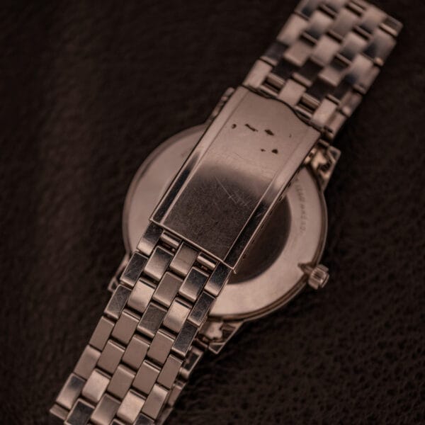 A close-up of the Longines Flagship Ref. 2821 wristwatch, featuring its sleek black "Pinstripe" dial and Cal. 285 movement, with the silver clasp side facing up on a dark textured surface.