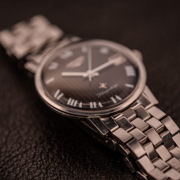 A Longines Flagship Ref. 2821 wristwatch with a black "Pinstripe" dial, Roman numerals, and Diamond Cal. 285 rests on a textured dark surface.