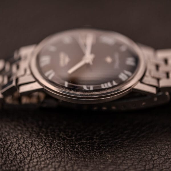 Close-up of the Longines Flagship Ref. 2821, featuring a black "Pinstripe" dial and diamond Cal. 285, with Roman numerals, displayed on a textured black surface.
