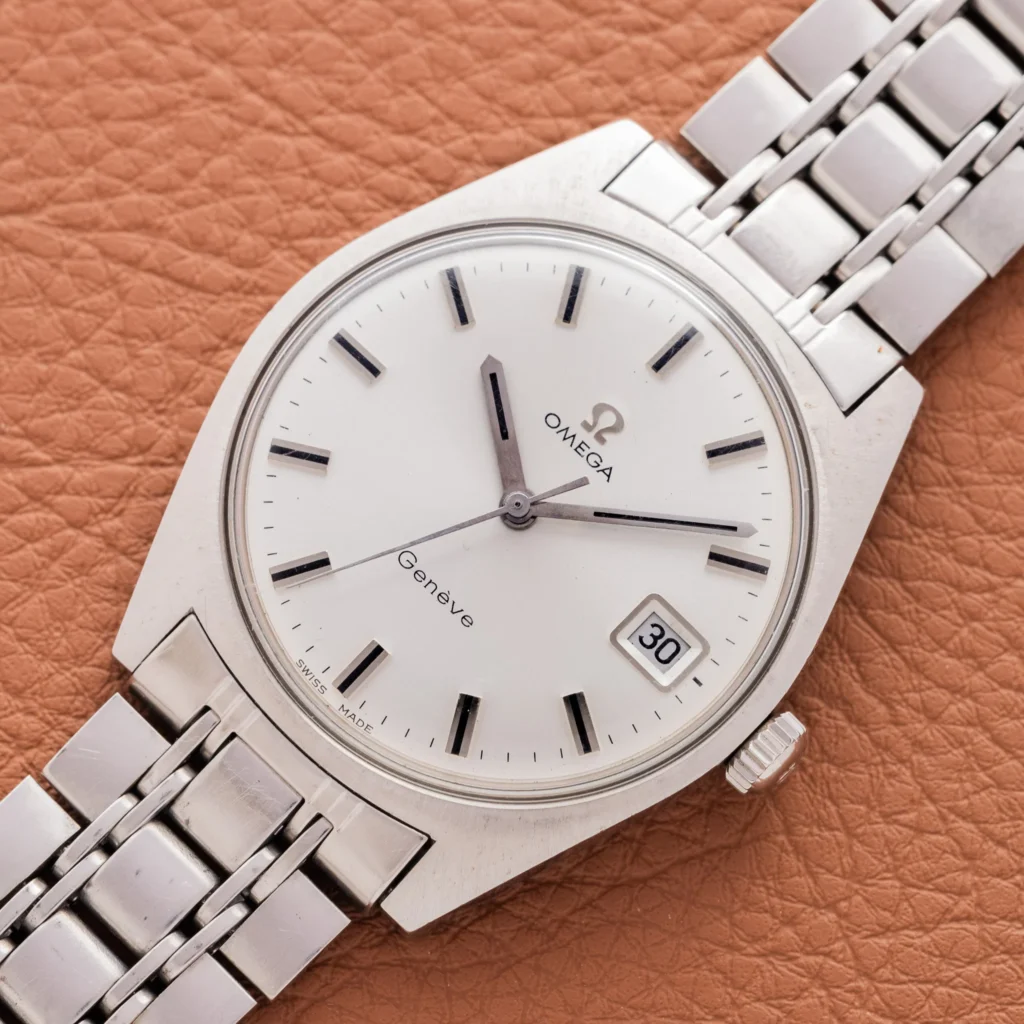 Silver Omega Genève 136.041 wristwatch with a white dial and metal band, displaying the date 30, set on brown leather.