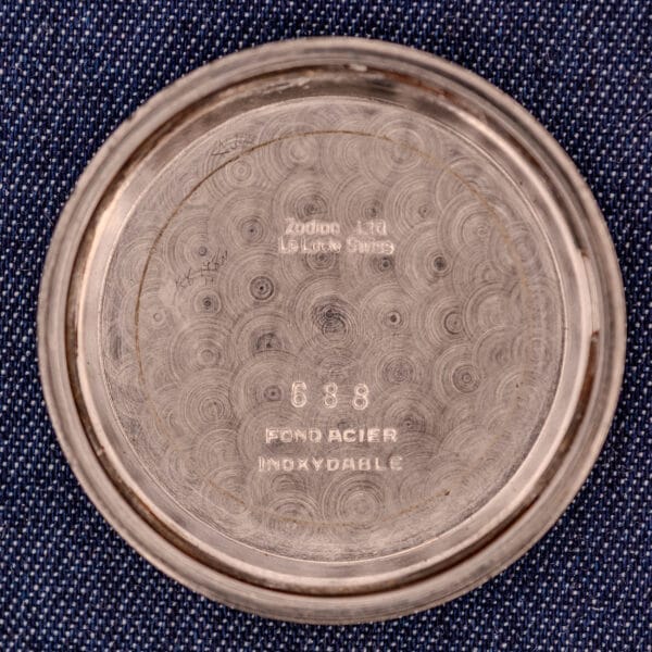 Inside case back of a Zodiac Glorious Automatic Tuxedo Dial Ref. 688 Cal. 1361, featuring engraved text and numbers on textured metal, shown against blue fabric.