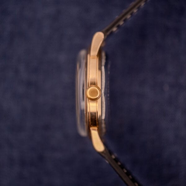 Side view of the Zodiac Glorious Automatic Tuxedo Dial Ref. 688 Cal. 1361, a gold wristwatch with a black strap, displayed on dark blue fabric and radiating elegant style.