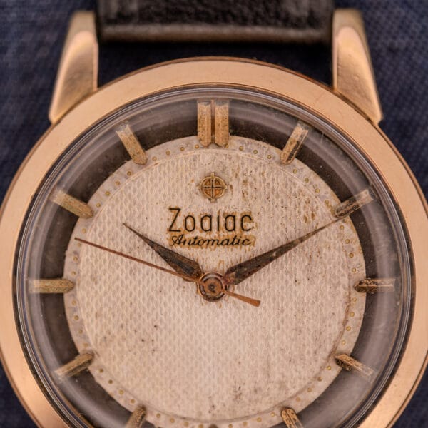 Close-up of a Zodiac Glorious Automatic Tuxedo Dial Ref. 688 Cal. 1361 wristwatch, showcasing its vintage appeal with a worn white dial, gold-tone case, and hands.