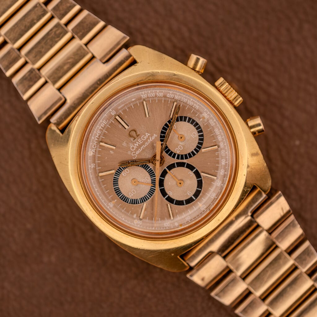 Omega Seamaster Chronograph Ref 145.029 with Cal. 861 movement and gold bracelet, featuring a brown dial, displayed on a brown textured surface.