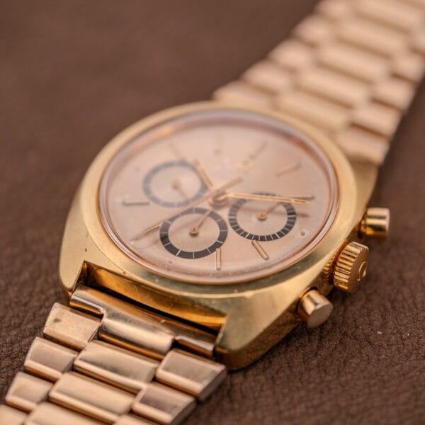 The Omega Seamaster Chronograph Ref 145.029 Cal. 861, featuring a gold case, metal band, and three subdials, is shown resting on a brown textured surface.