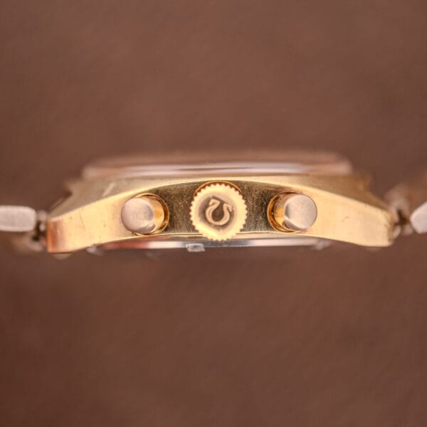 Side view of the gold Omega Seamaster Chronograph Ref 145.029 with two pushers, crown, and Cal. 861 movement, set against a brown background.