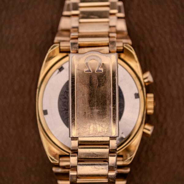 Close-up of the Omega Seamaster Chronograph Ref 145.029 Cal. 861 gold watch bracelet and clasp with Omega logo, showing refined details against a brown background.