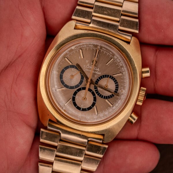 An Omega Seamaster Chronograph Ref 145.029 Cal. 861 wristwatch with a brown dial and three subdials is held in a person's hand.